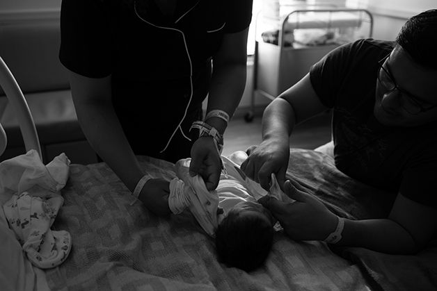 New parents changing newborn's clothing.  Baby is laying on the hospital bed.