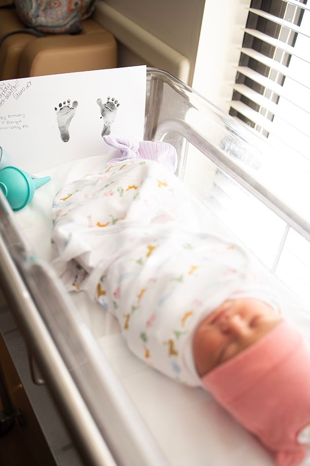 Newborn baby girl laying in her bassinet.  Focus is on her footprints at the bottom of her bassinet.