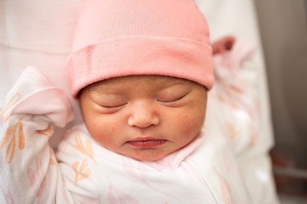 Newborn baby girl in pink and white onesie sleeping in her bassinet.