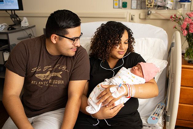 New parents sitting on the hospital bed, mom is holding newborn baby girl.