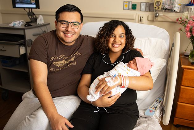 New parents sitting in the hospital bed smiling and holding their newborn baby girl.