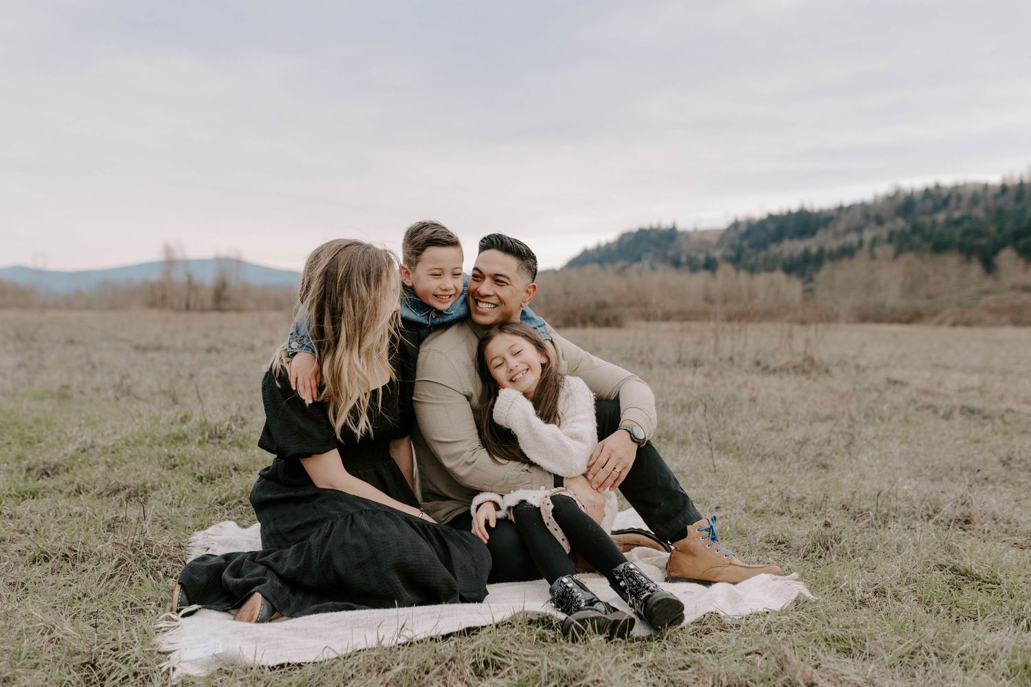 Couple sharing intimate moment while sitting on blanket in rustic field setting.