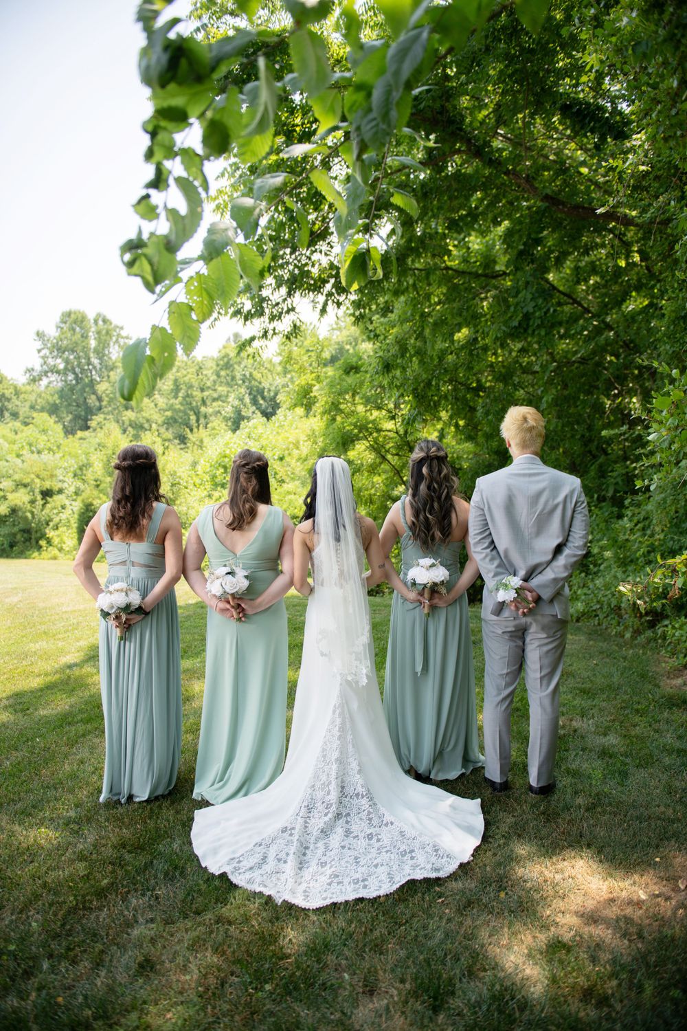 Wedding party in sage green dresses and gray suits posed in garden setting.