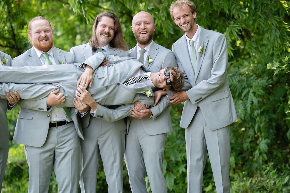 Groomsmen in light grey suits pose together outdoors for wedding party photos.