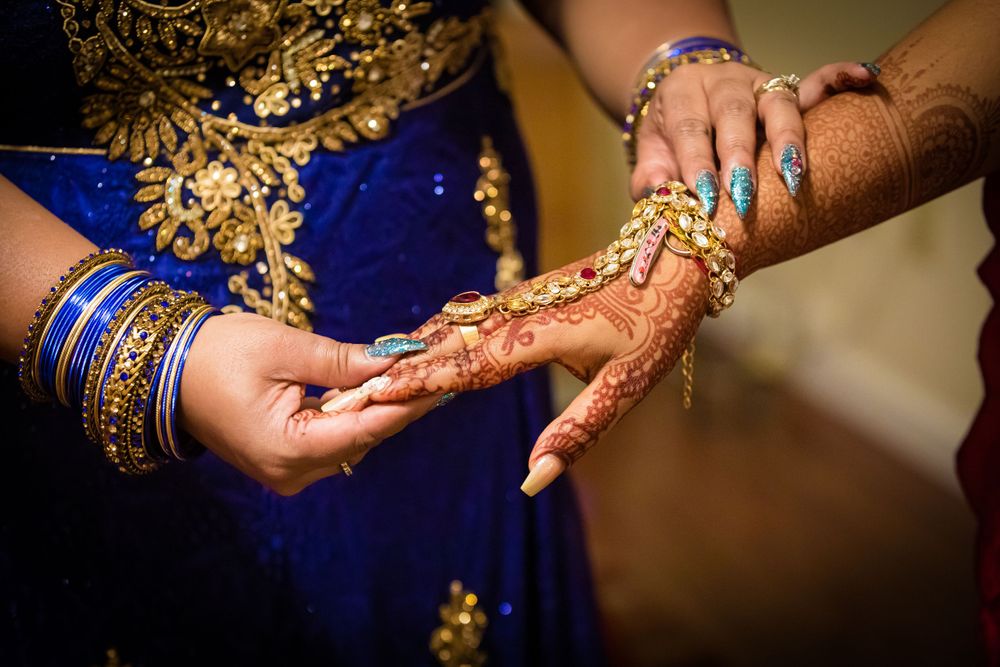 Detailed shot of hands with mehndi designs and gold jewelry against blue fabric.