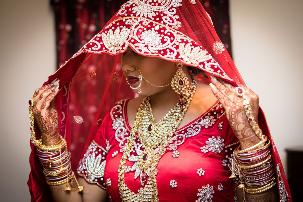 Traditional Indian bride in red embroidered wedding attire with gold jewelry.