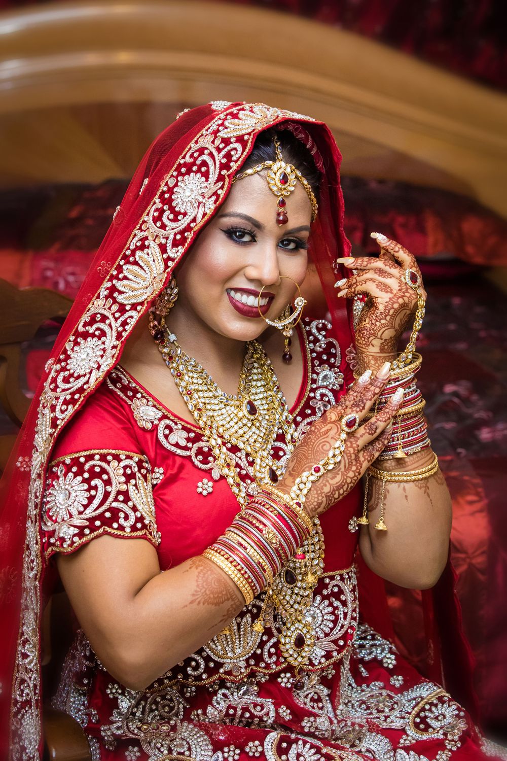 Traditional Indian bridal attire with gold jewelry and red embroidered lehenga.