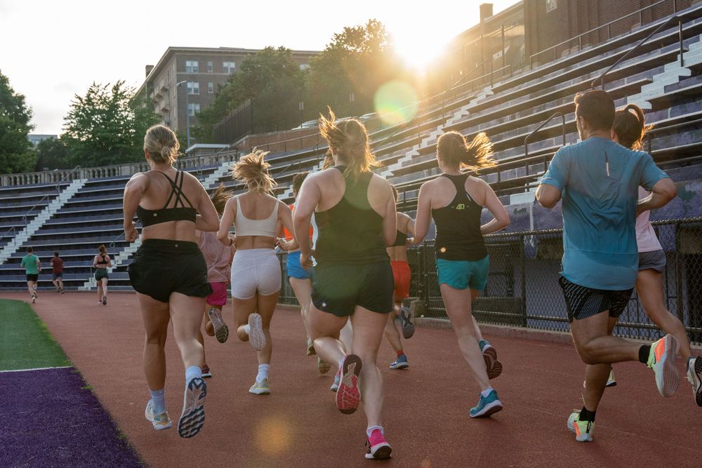 Group of runners training together on a track during sunset with stadium bleachers in the background.