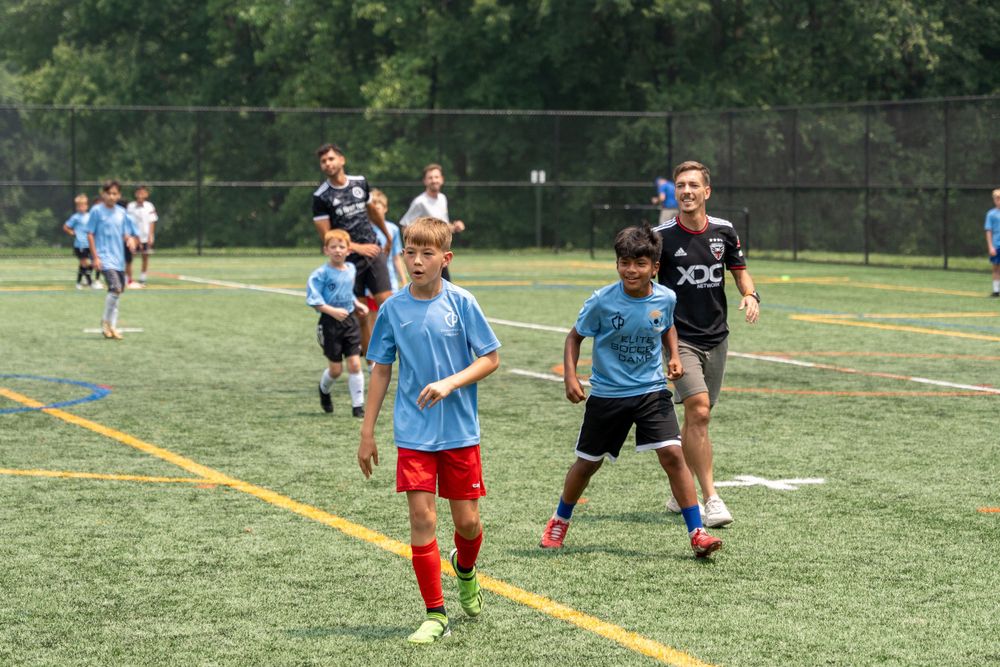 Soccer players in light blue and red uniforms practicing on an outdoor turf field.