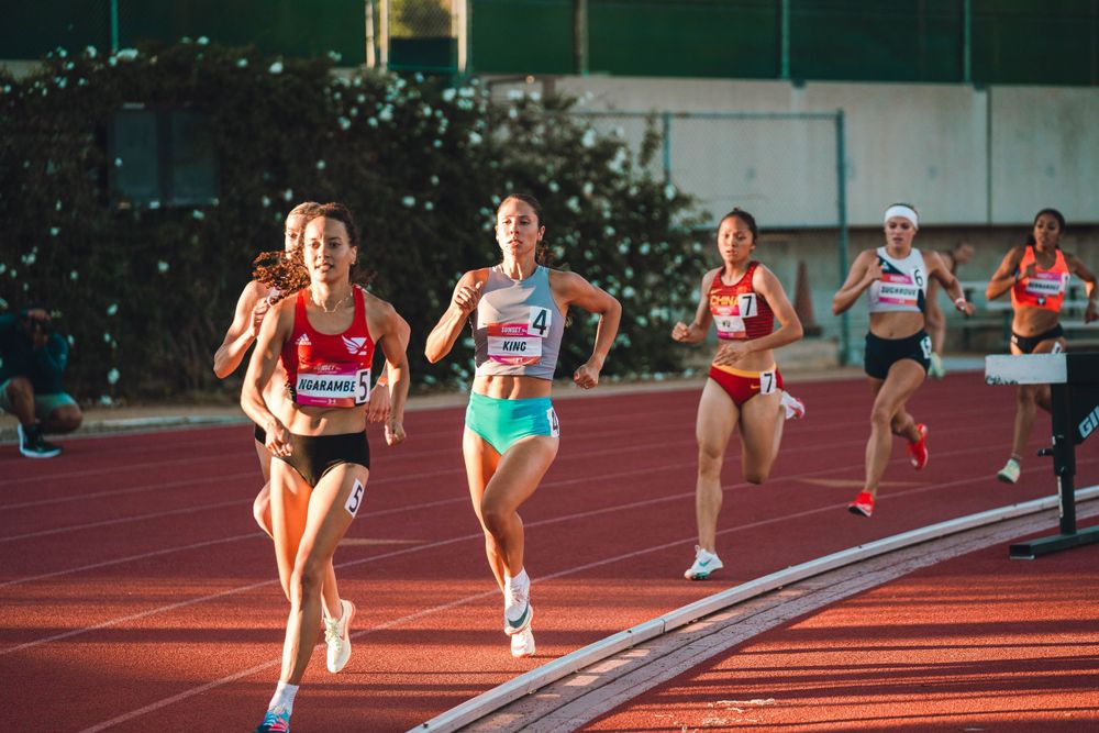 Athletes compete in a track race at sunset on a red running track.