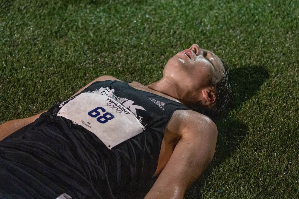 Exhausted athlete lying on grass after training, wearing a race number bib.