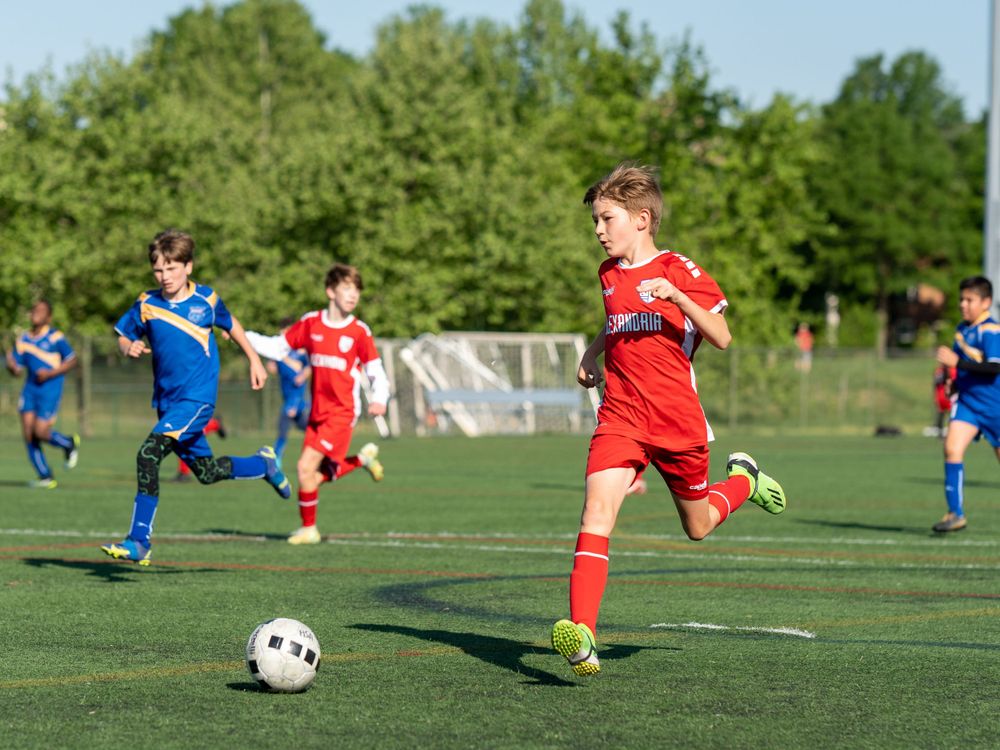 Youth soccer players competing for ball during match on grass field.