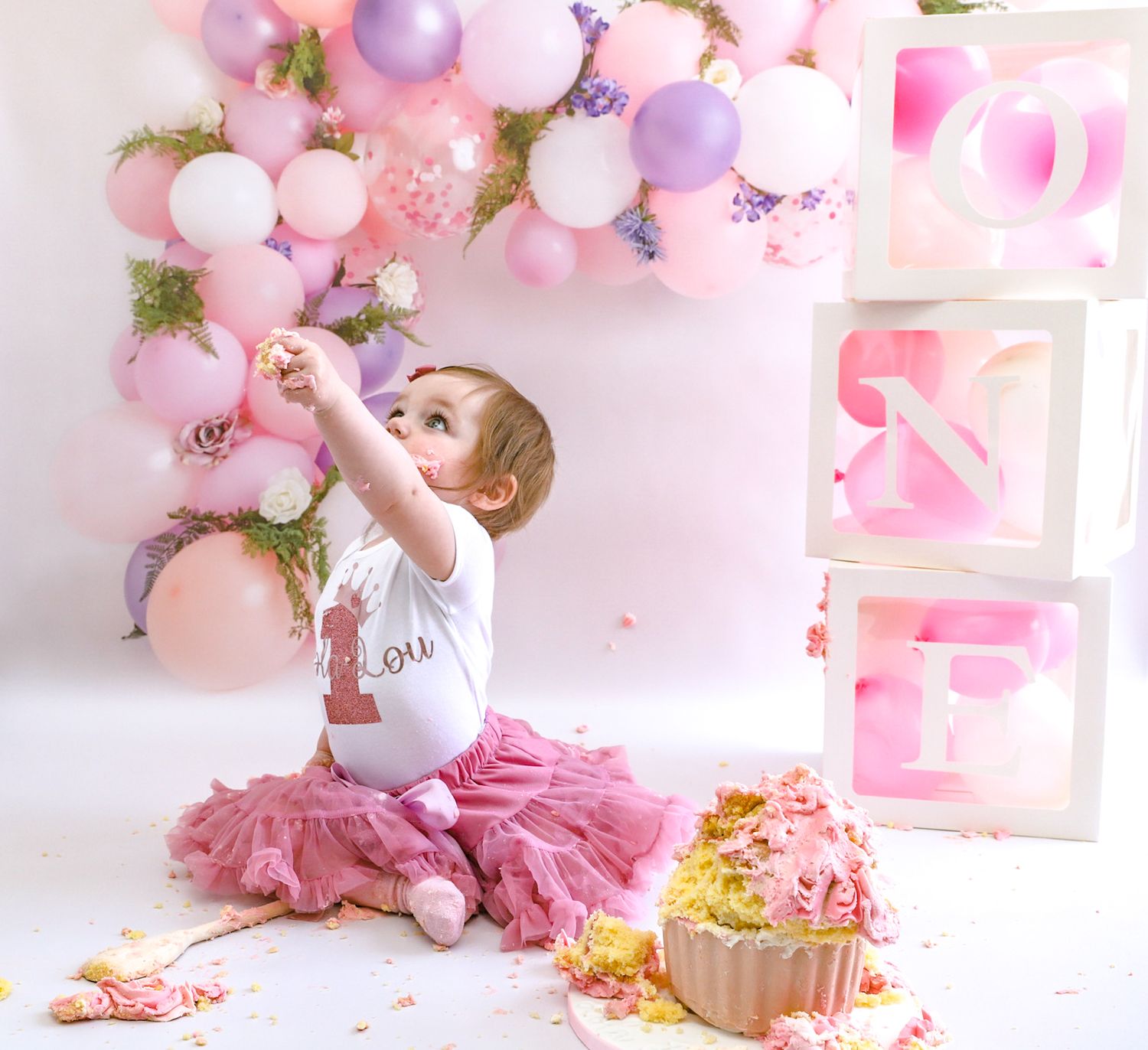 First birthday cake smash photo session with pink and purple balloon decorations.