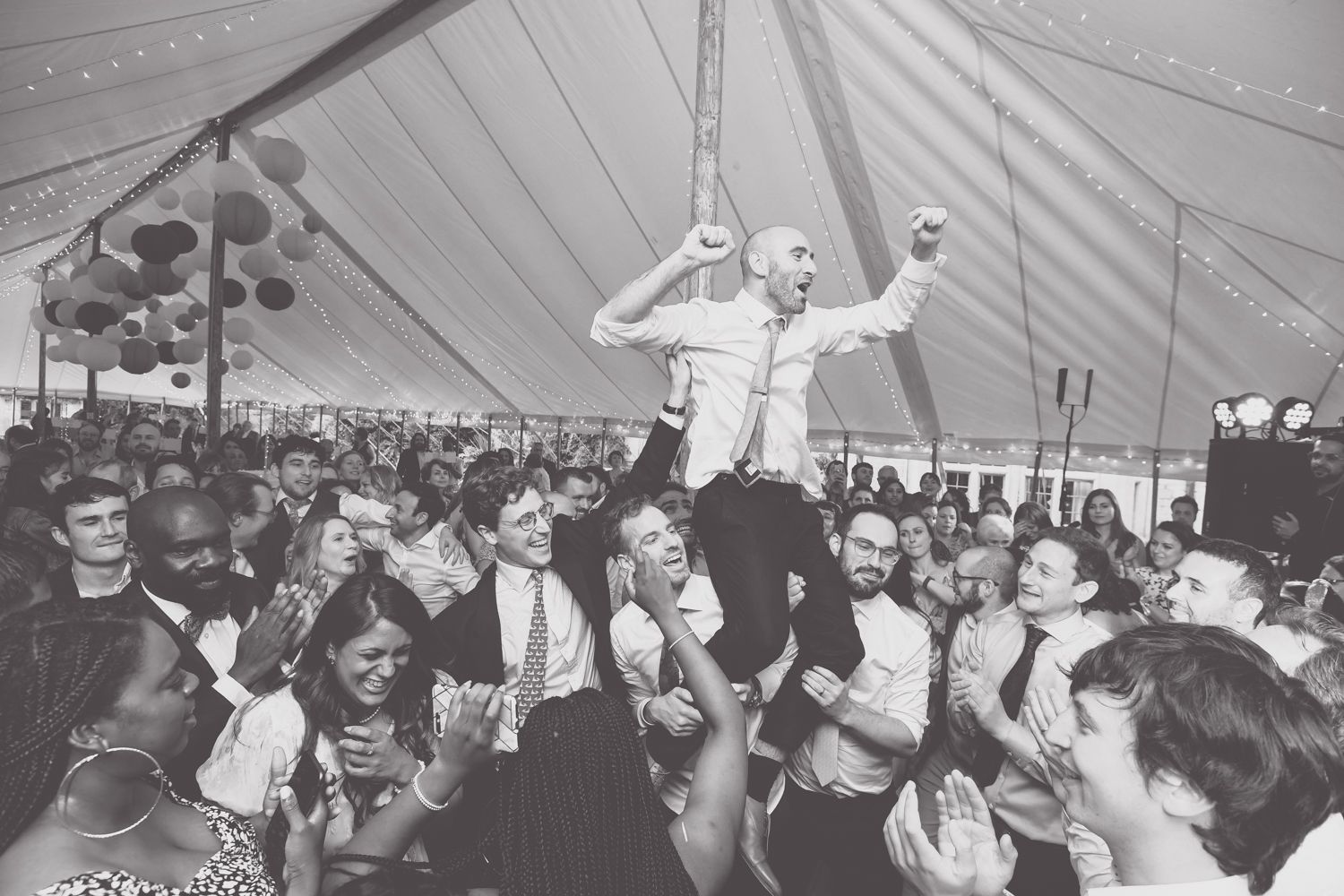 Black and white photo of wedding celebration with dancing guests under a tent.