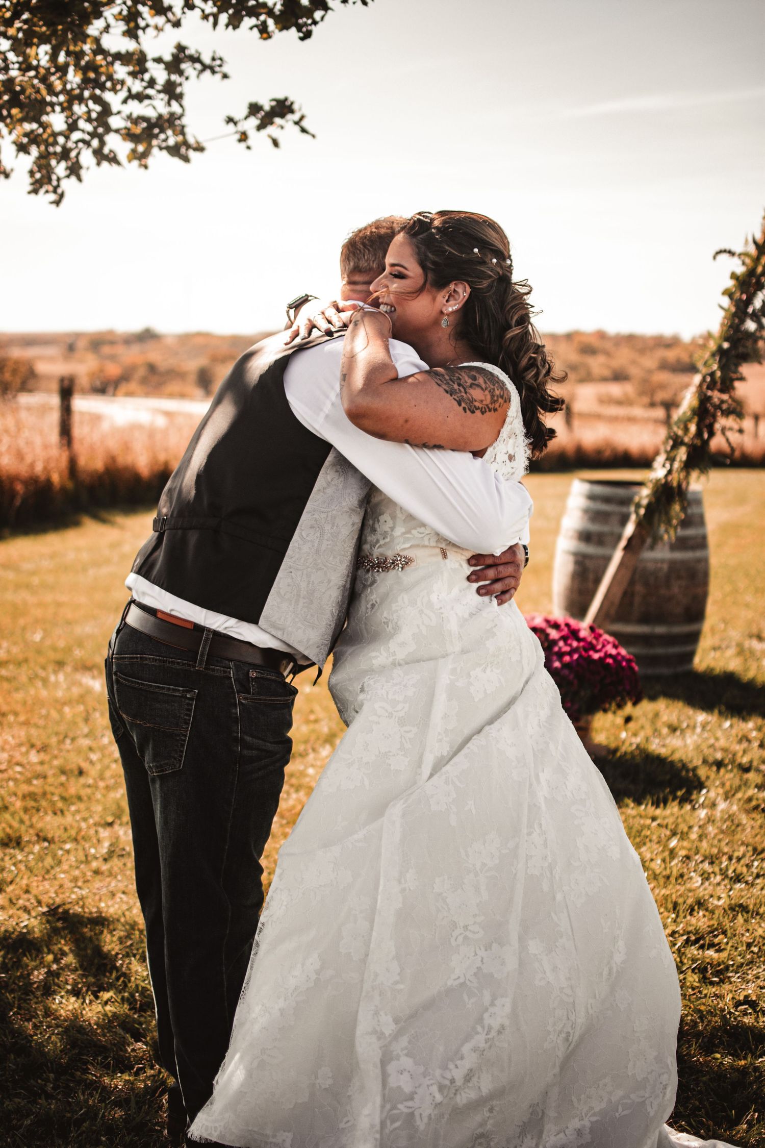 Wedding couple embracing outdoors at sunset in a rustic countryside setting.