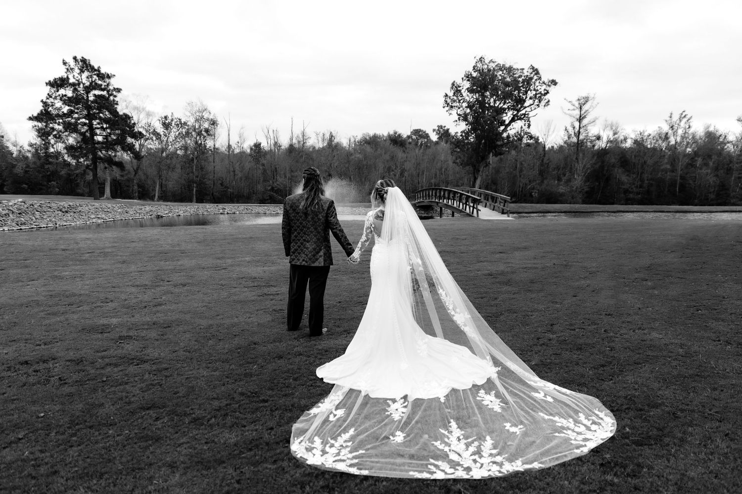 A dramatic black and white shot of newlyweds with a flowing cathedral veil on expansive grounds.