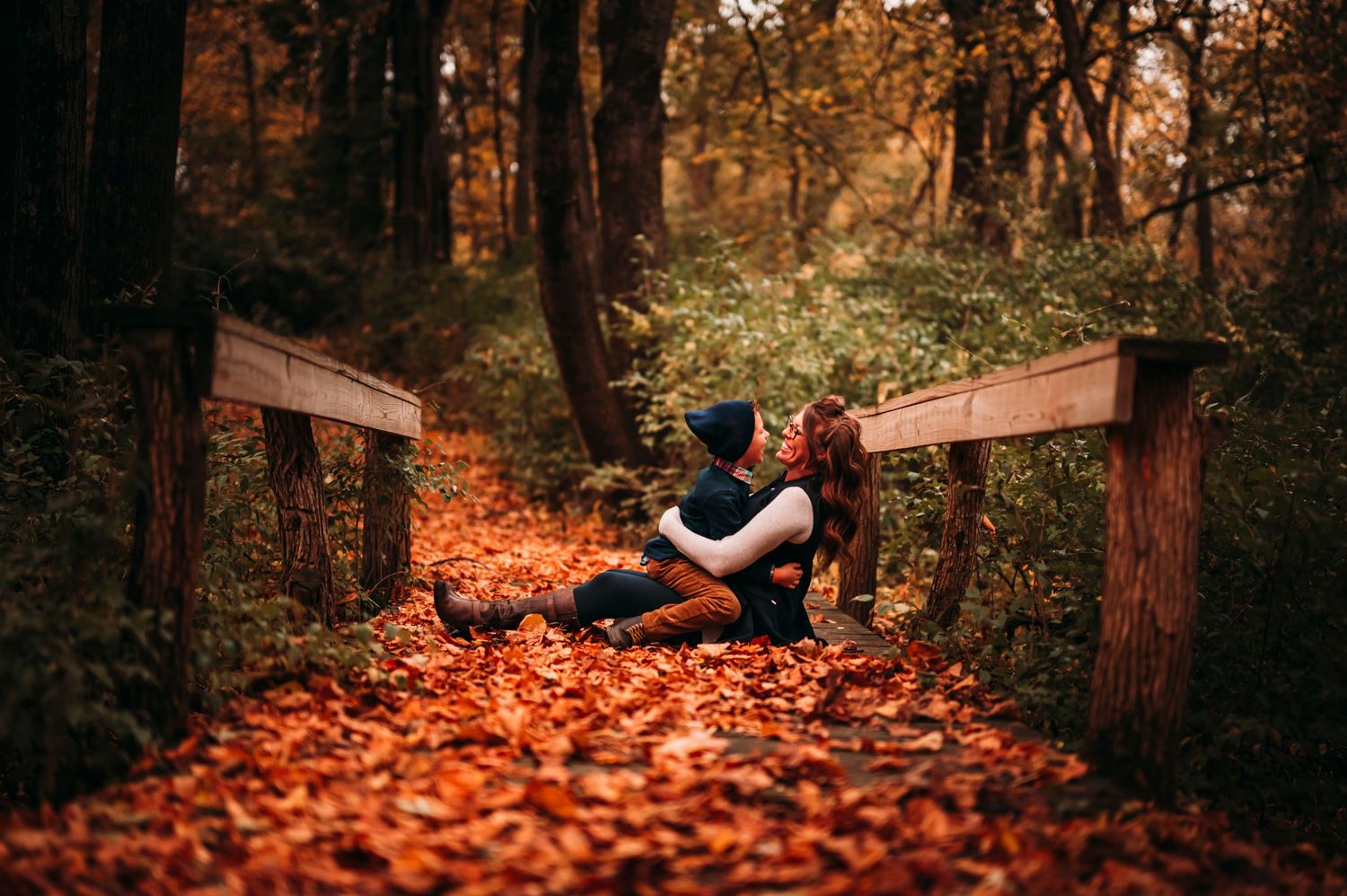 Couple sharing a romantic kiss sitting on fall leaves in a forest.