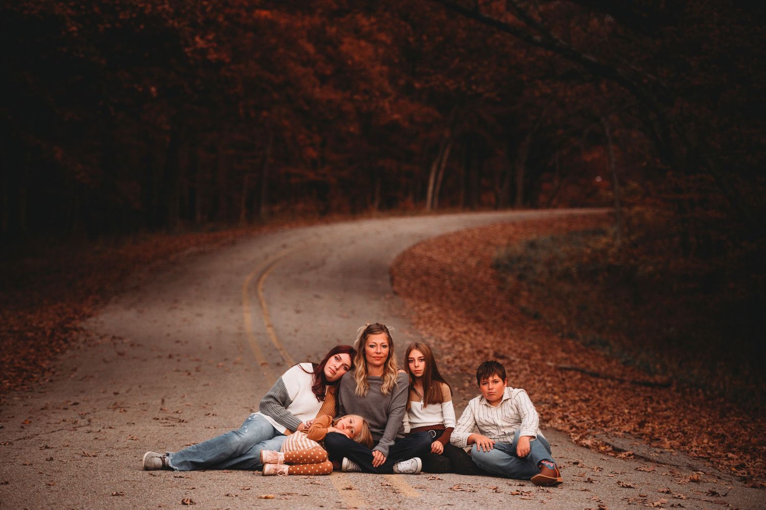 Four friends sitting together on a winding road surrounded by autumn foliage.