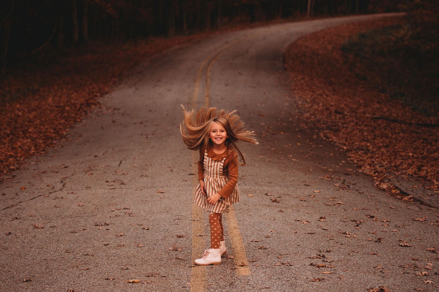 Young girl joyfully tossing her hair on a scenic autumn road.