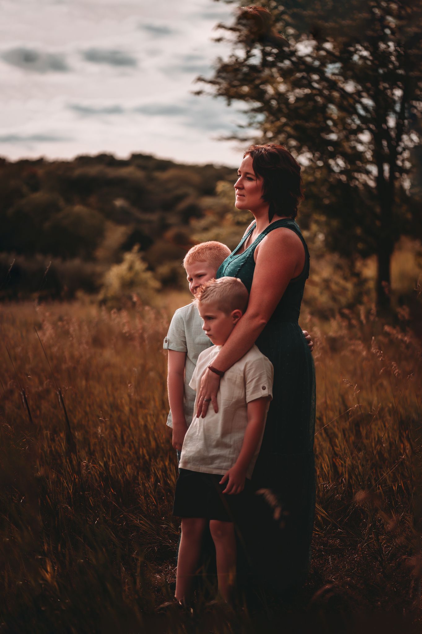 Mother standing in a golden field with her two young blonde sons hugging her closely.