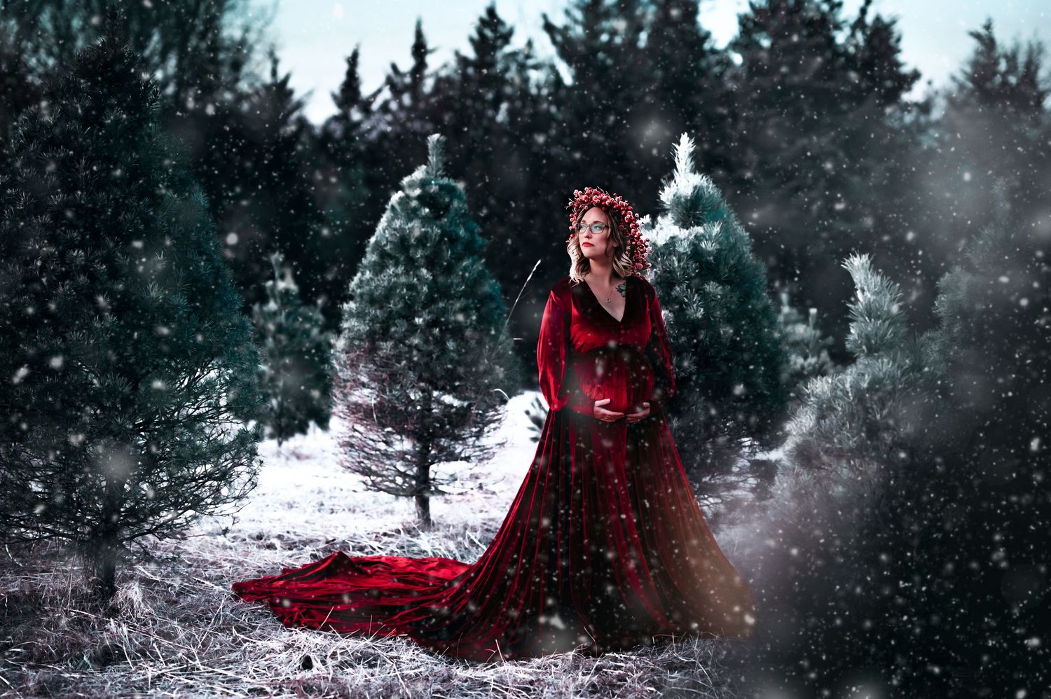 Woman in elegant red gown standing among snow-covered Christmas trees in a magical winter wonderland scene.