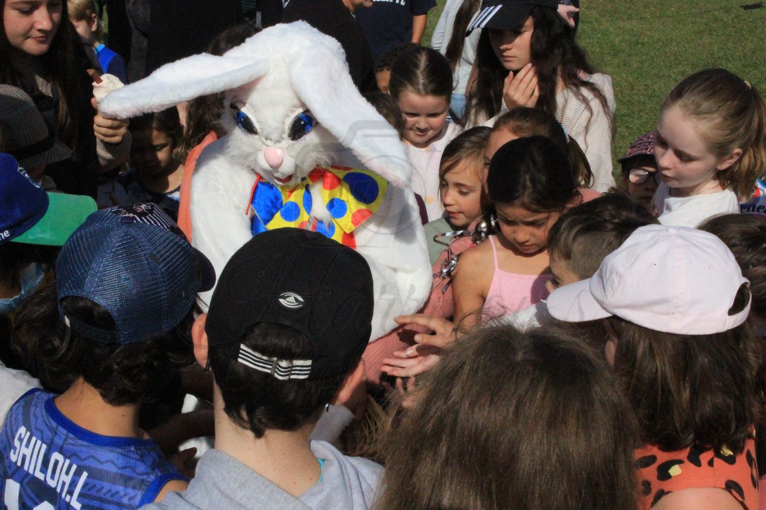 Children crowding around Easter Bunny mascot in colorful costume at outdoor Easter event.