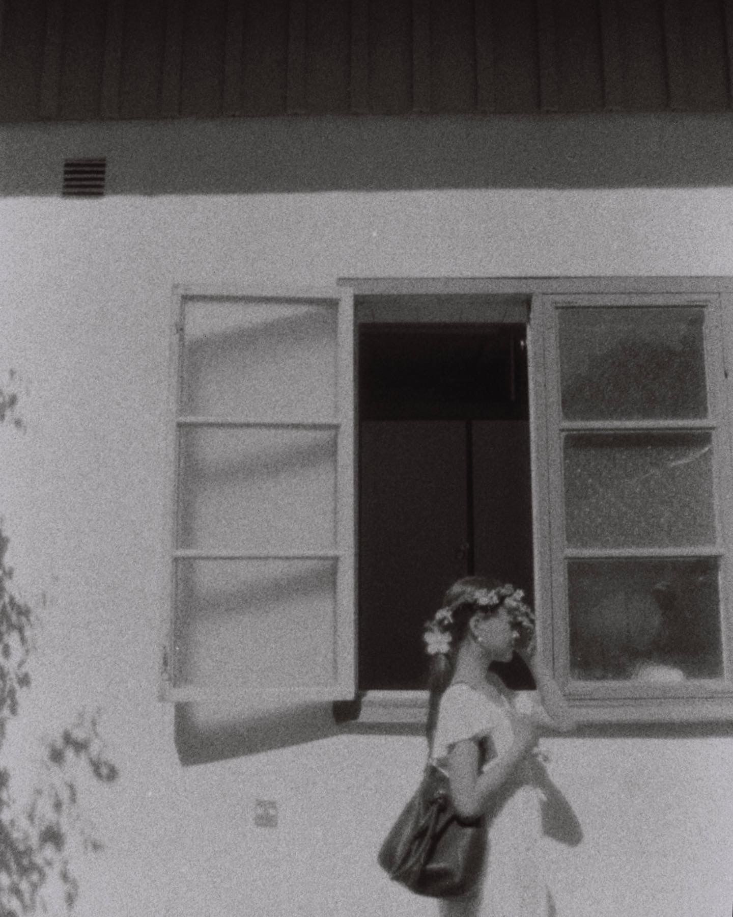 A vintage black and white photo of someone standing by an open window with shutters.