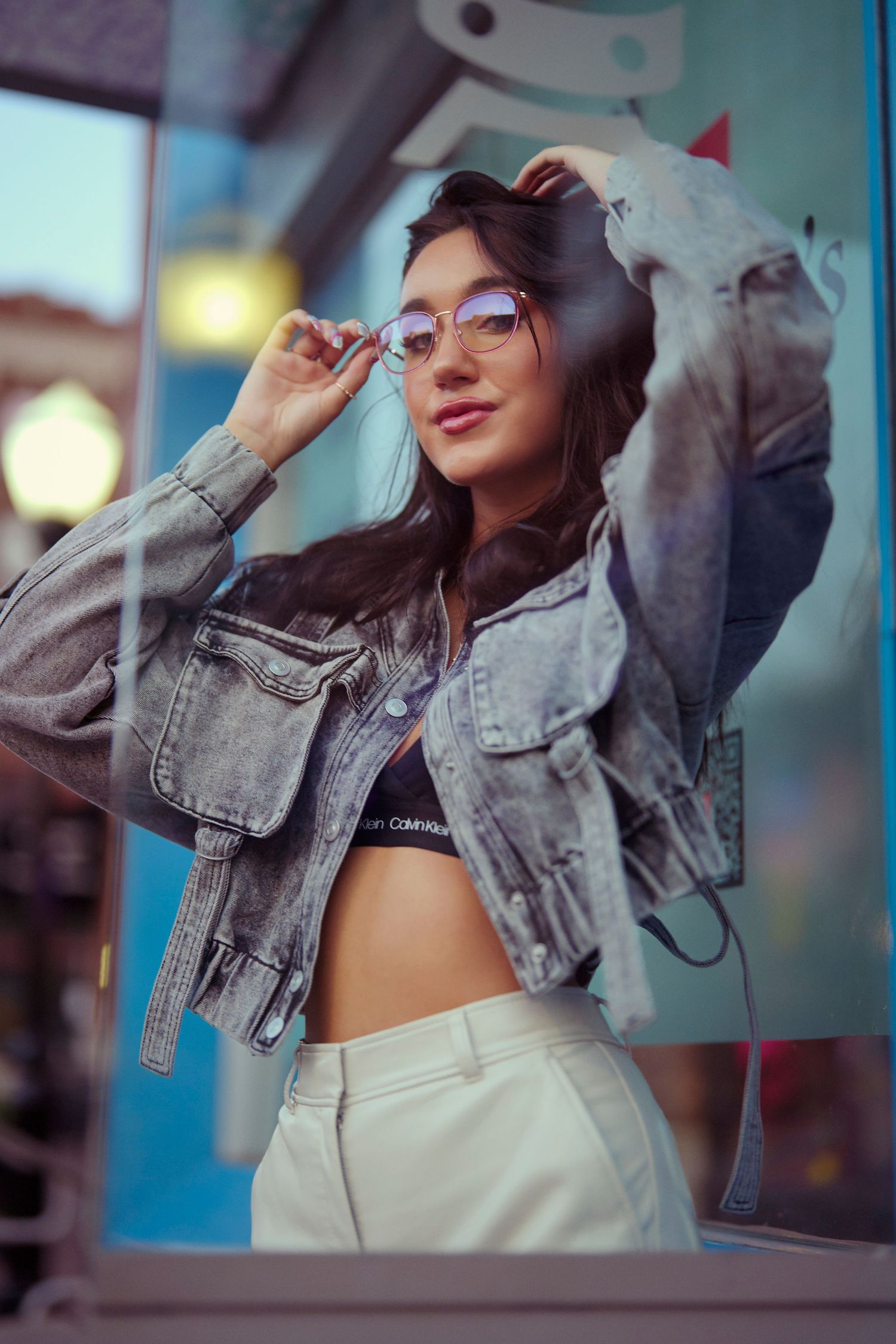 Urban fashion portrait with denim jacket and glasses against colorful city backdrop.