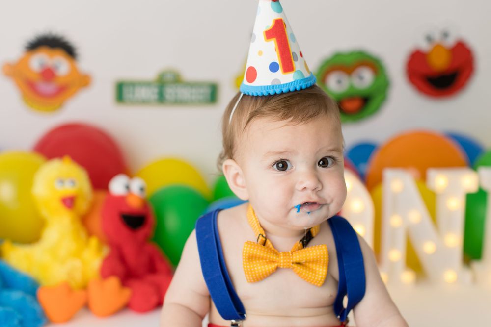 Baby in party hat and bow tie smiling at first birthday celebration.