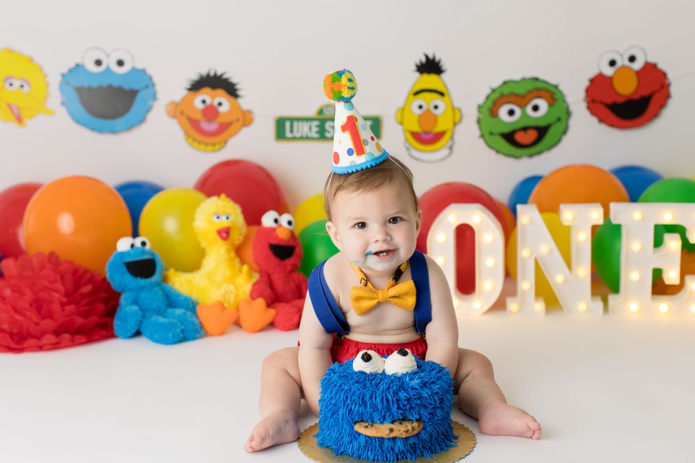 Baby in blue and red outfit surrounded by Sesame Street characters and ONE letters.