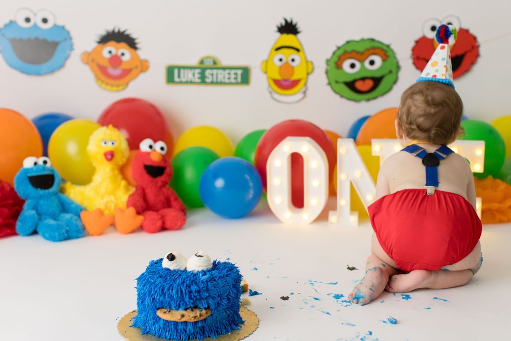 Behind view of baby reaching for blue monster cake at birthday party.
