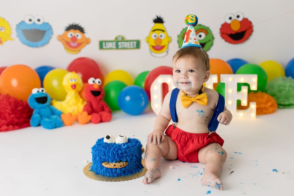 Baby sitting with Cookie Monster cake amid Sesame Street themed decorations.