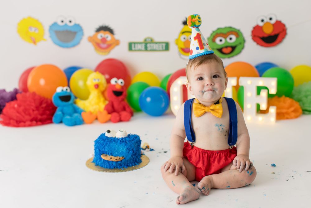 Baby in suspenders smiling at Sesame Street themed first birthday party.