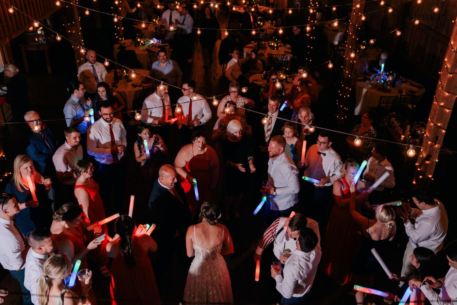 Wedding reception dance floor filled with guests celebrating under warm glowing lights.