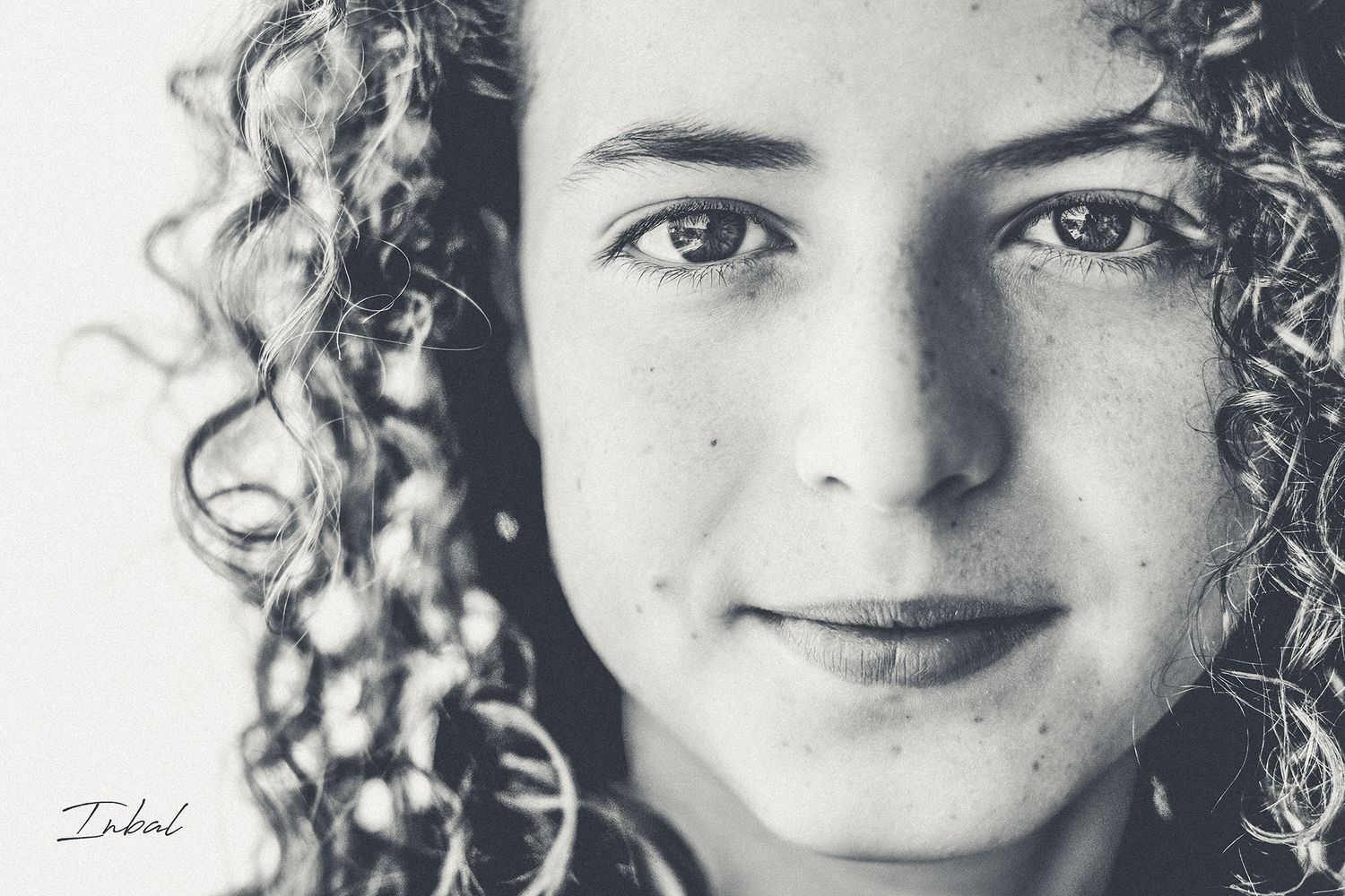 Black-and-white close up photo of a child with long curly hair looking at the camera.