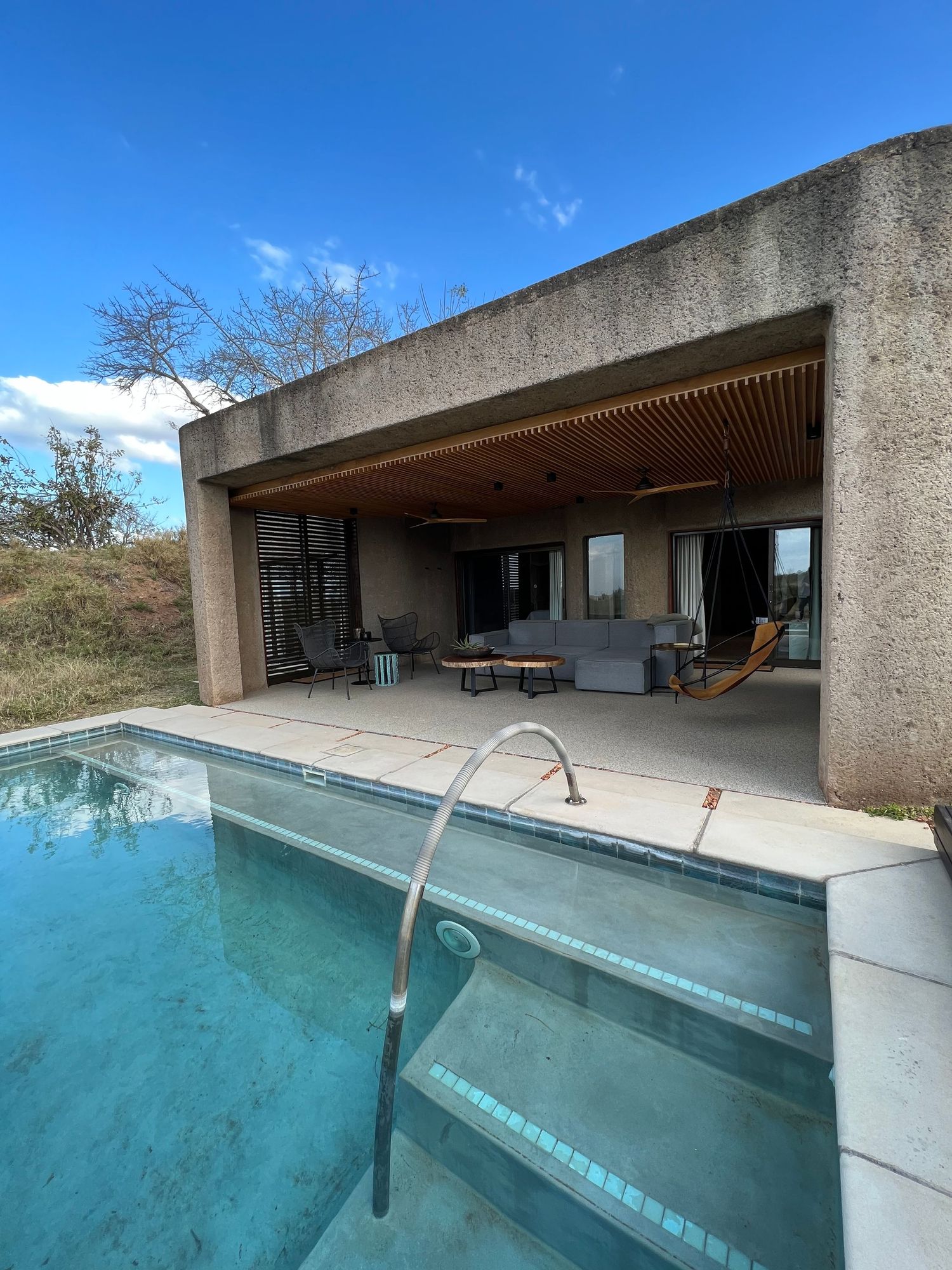 Modern poolside terrace with infinity pool and covered lounge area featuring concrete architecture.