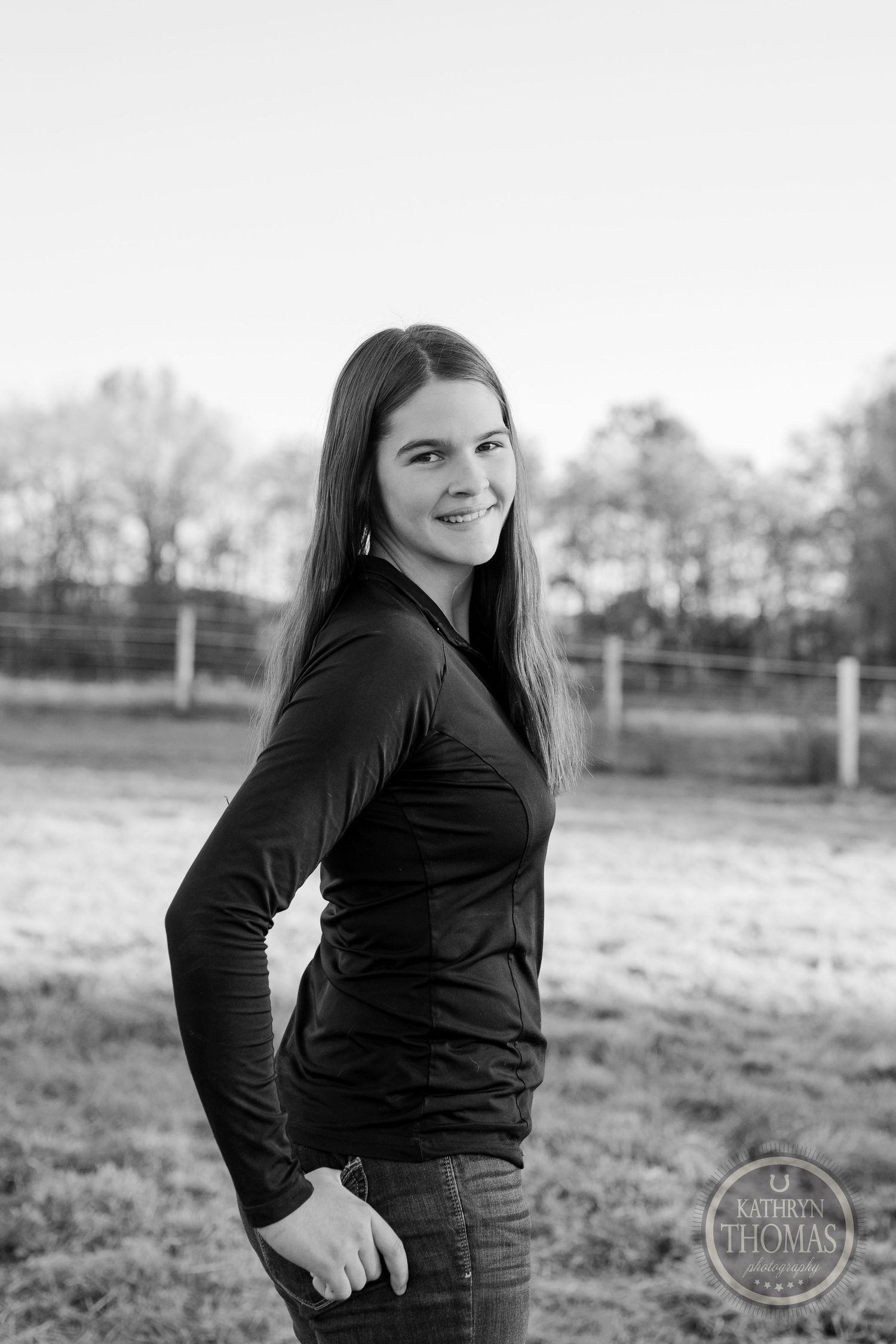 Black and white portrait in rural setting with fence line visible behind.