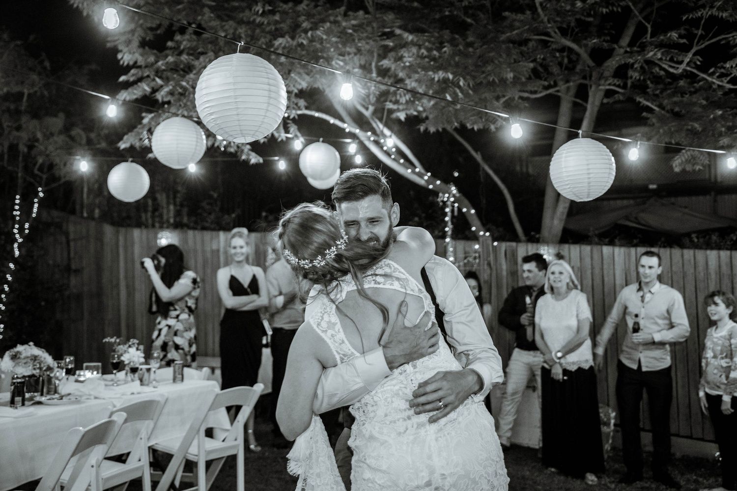 Black and white reception photo with paper lanterns and string lights creating romantic atmosphere.