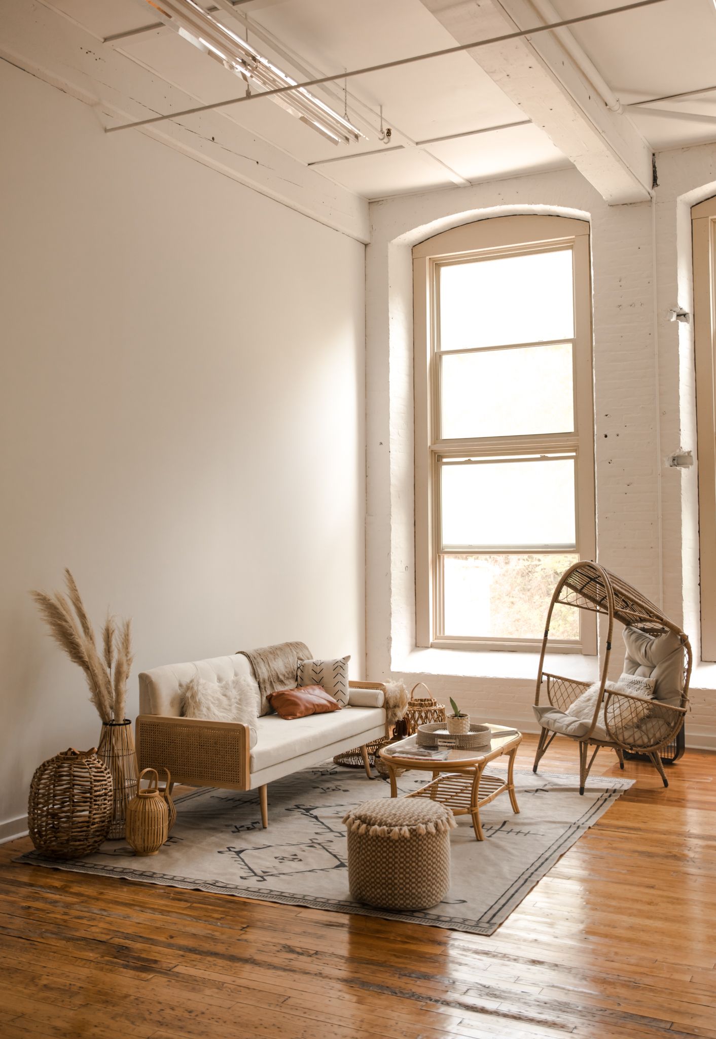 Minimalist boho living room with white walls, natural light, and wicker furniture on hardwood floors.
