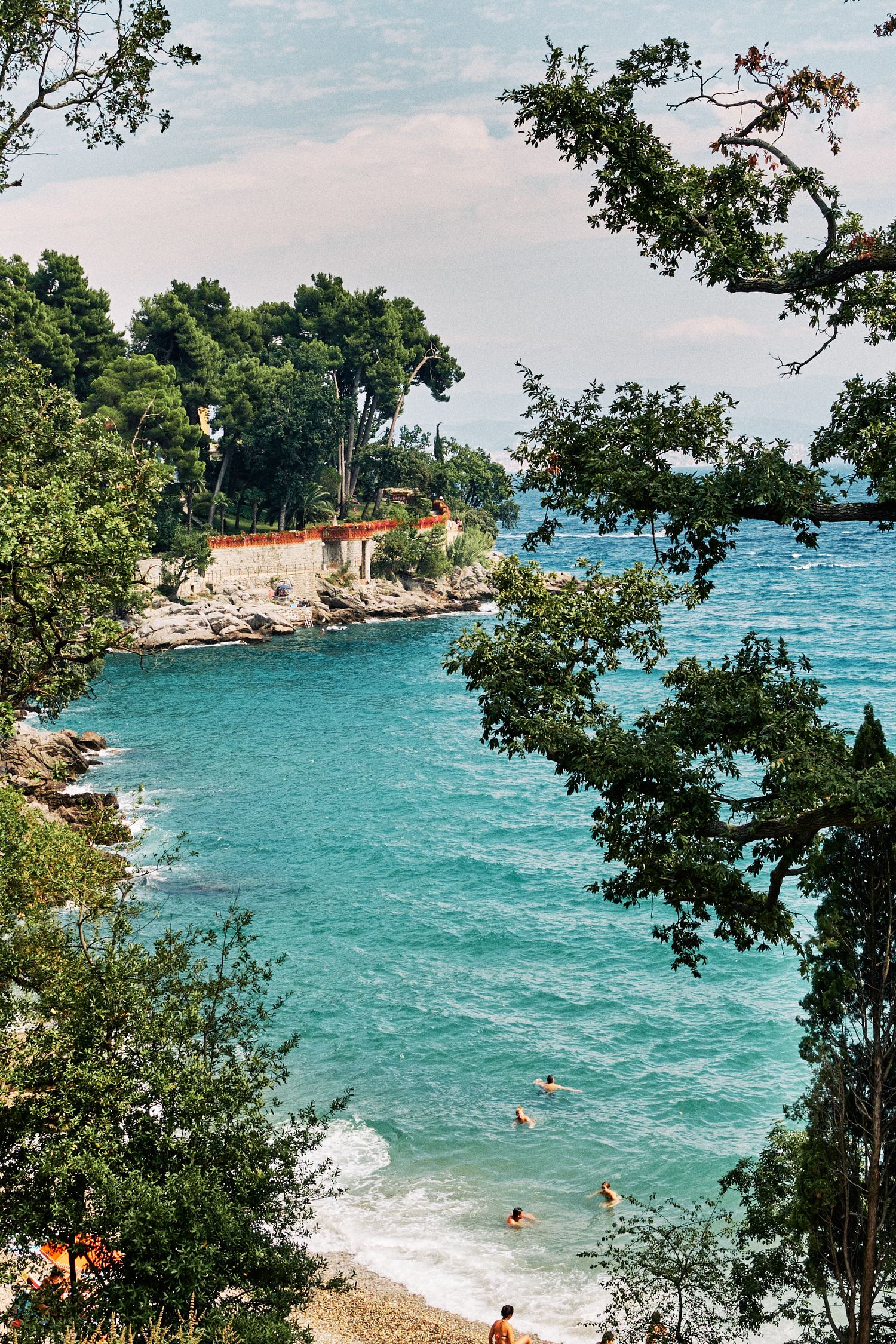 Turquoise beach cove framed by trees and rocky cliffs in Mediterranean setting.
