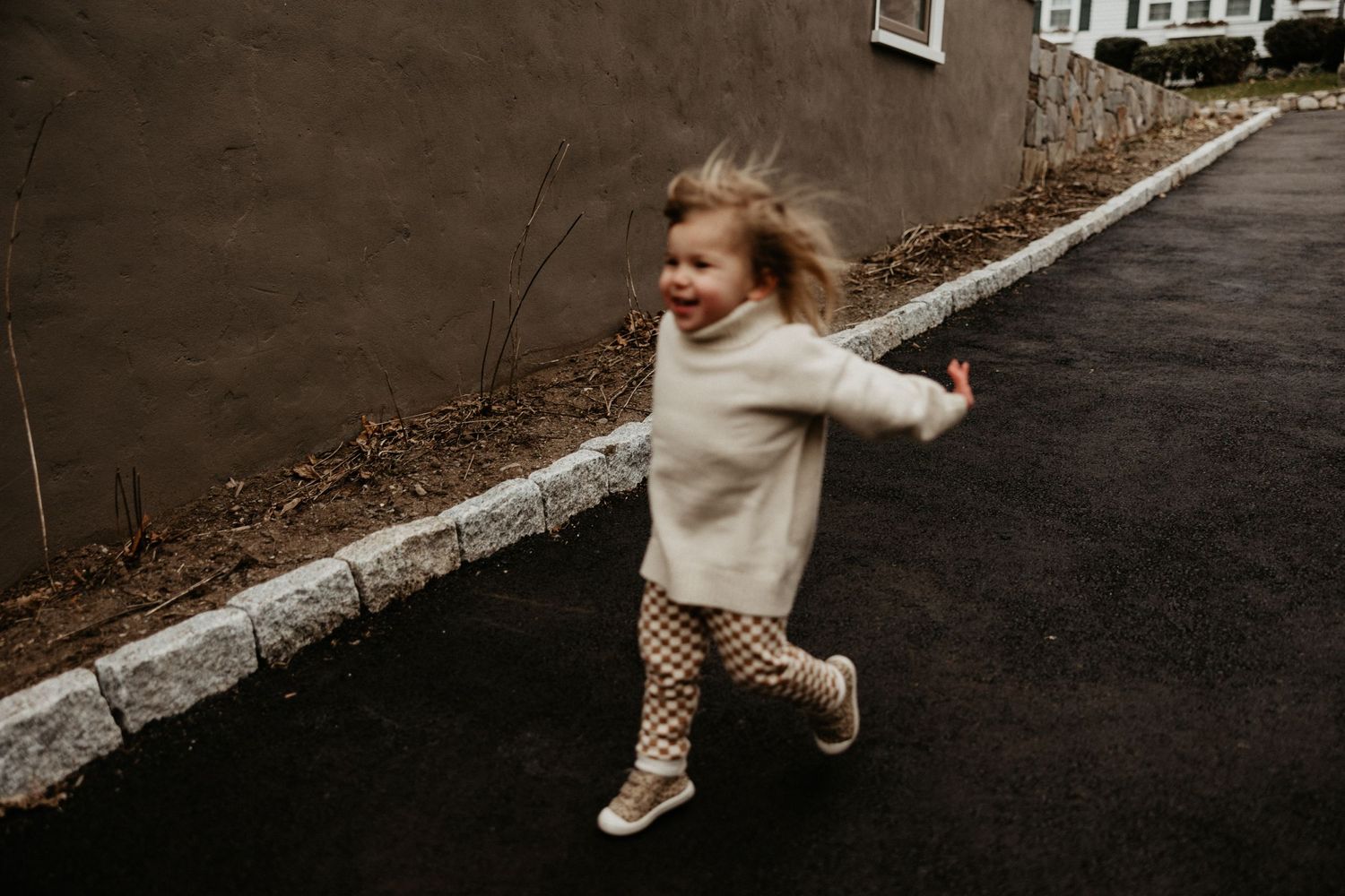 Happy young girl with flowing hair runs joyfully along a paved outdoor path near a wall. Arlington, Ma Miranda Photo & Co