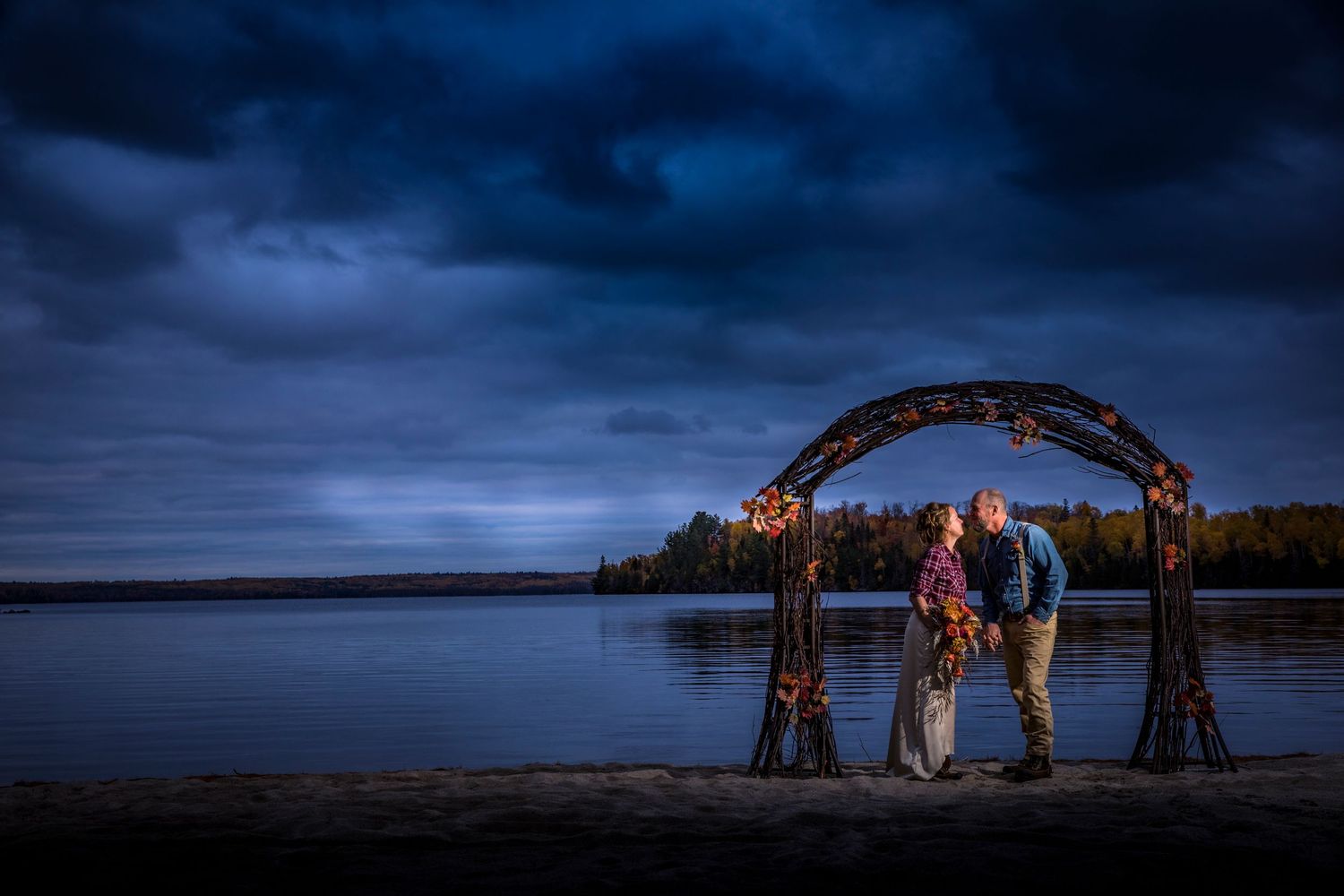 Dramatic sunset wedding ceremony under arched structure by lakeside.