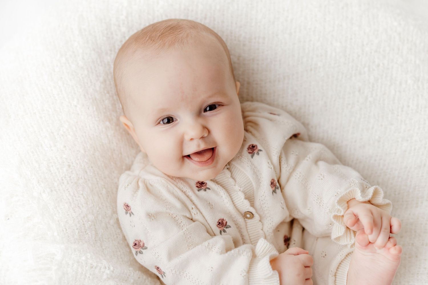 Baby in floral outfit smiling and laying on white background.
