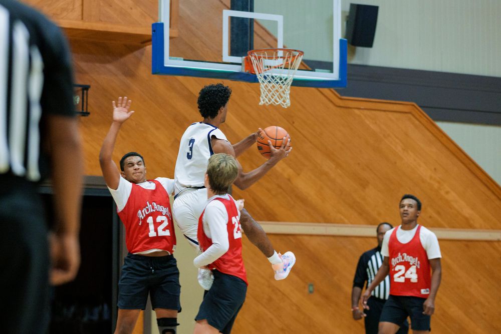 Basketball players leap for a rebound during an intense indoor game on a wooden court.