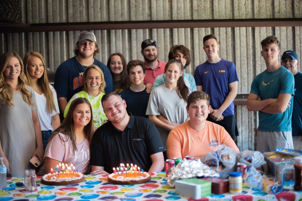 A group celebrates around a decorated table with birthday cakes and colorful party decorations.