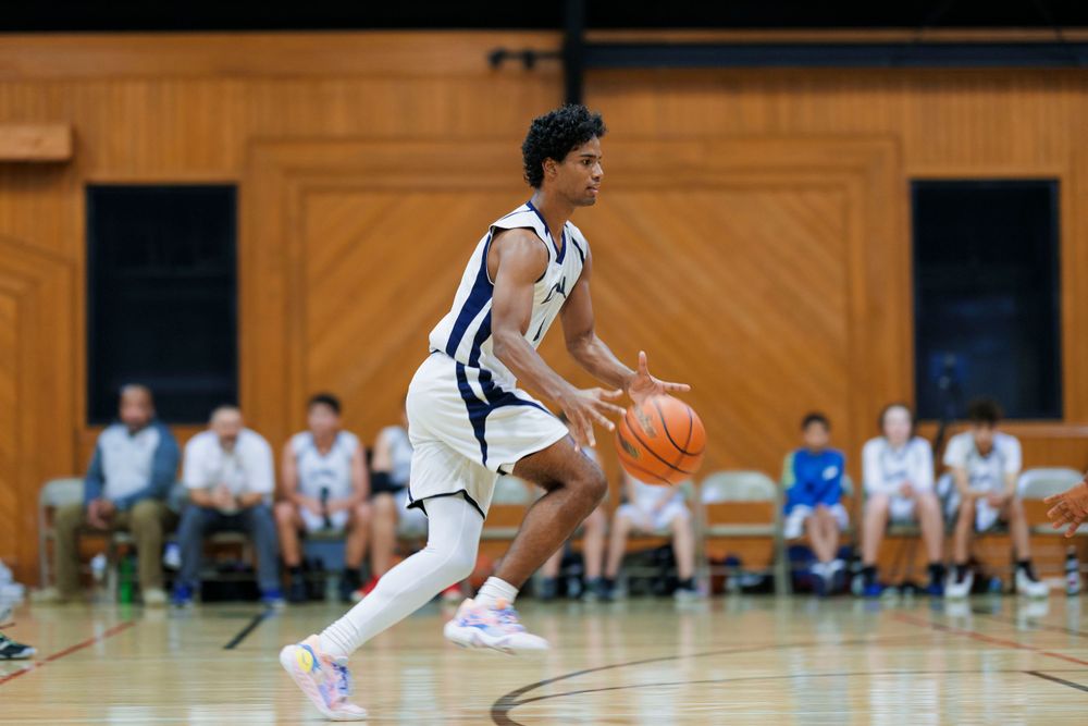 Basketball player dribbles across the court in a white uniform during a competitive game.