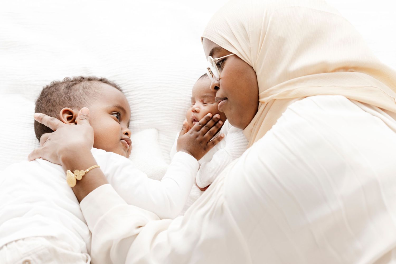 A tender maternal moment captured on white bedding showing gentle interaction and care.