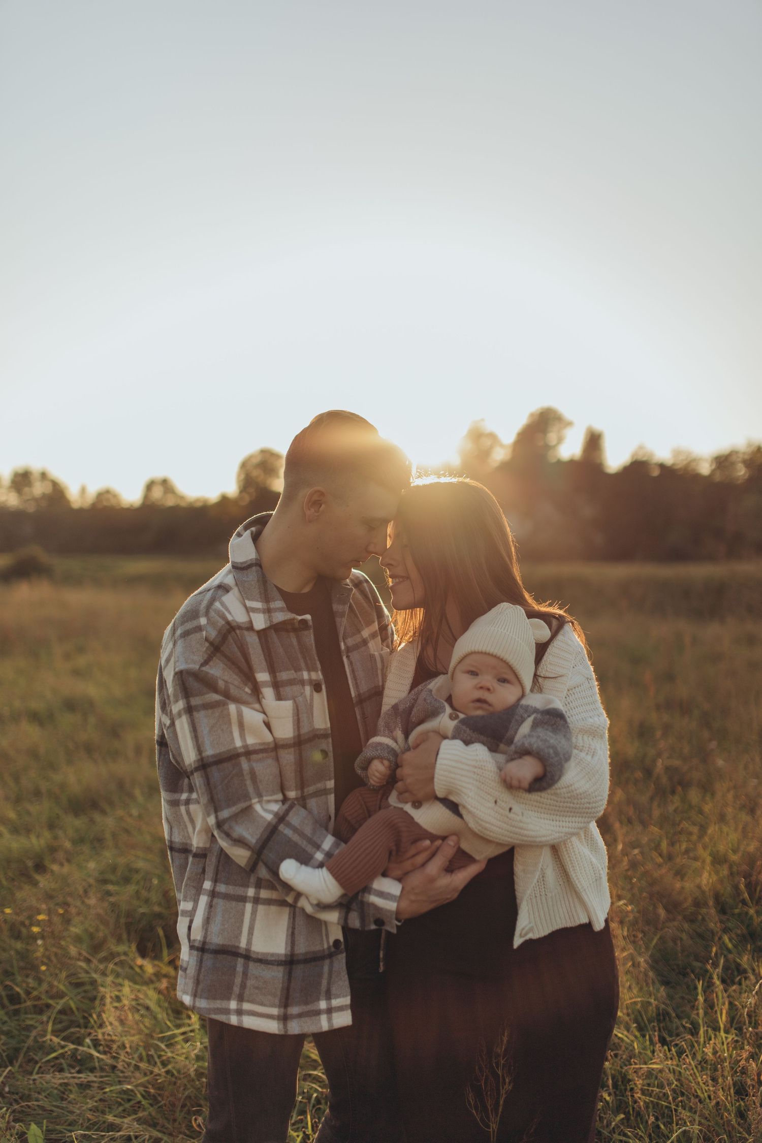Family sharing tender moment in sunlit field during golden hour.
