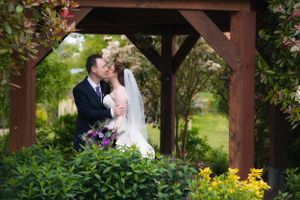 Wedding couple embraces under a wooden pergola surrounded by lush garden greenery.