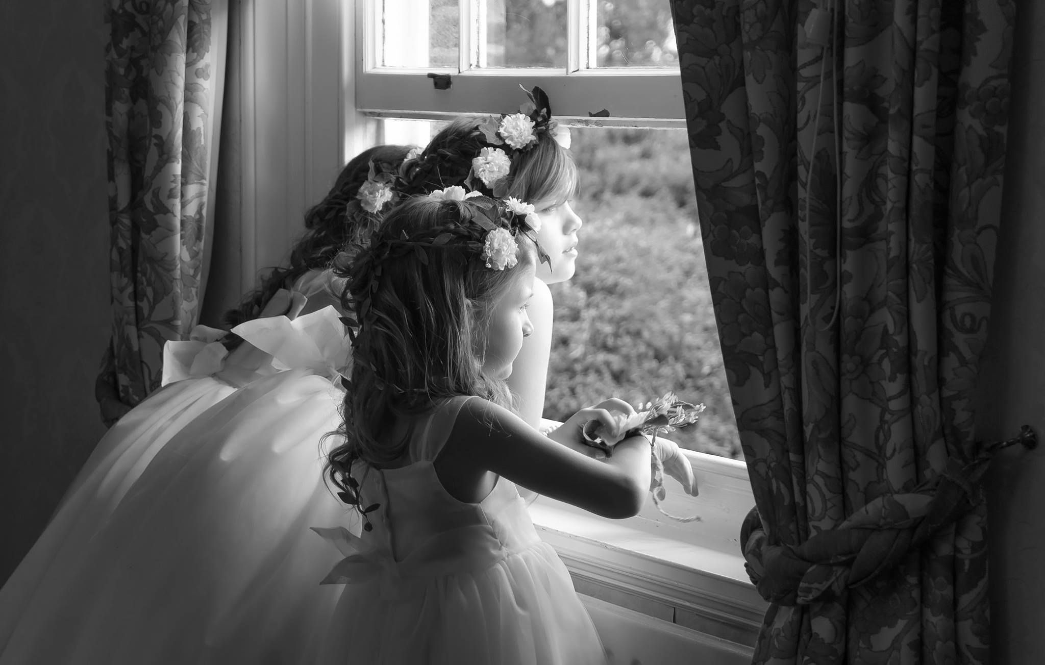 A dreamy black and white photo of a bride in a full tulle gown gazing through a window with soft light.